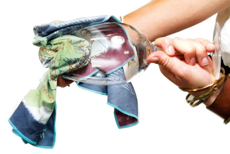 Person polishing a wine glass using a colorful map-printed cloth, with focus on hand, fabric detail, and glass clarity.
